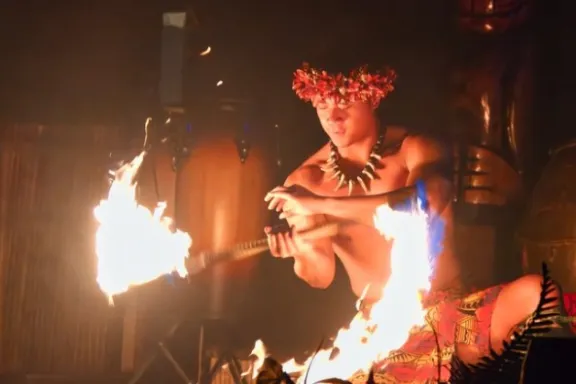 Performer with flower headdress skillfully twirling fire sticks.