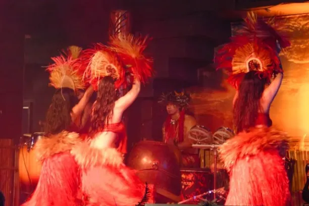 Dancers in red costumes perform in front of musicians with a sunset backdrop.