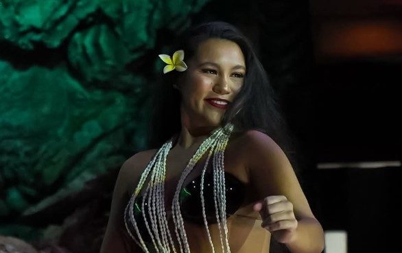 Woman dancing in traditional attire with beaded necklaces and flower in hair.