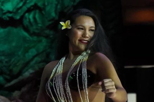 Woman dancing in traditional attire with beaded necklaces and flower in hair.