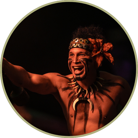 Smiling person with tribal face paint and necklace pointing forward.